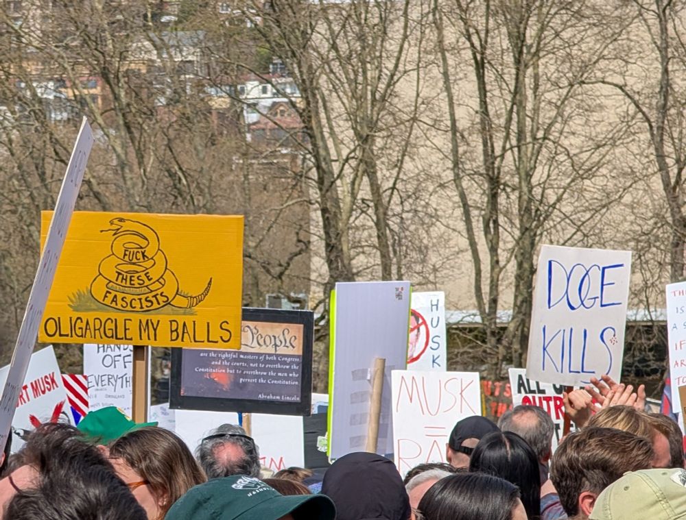 Protest signs at Seattle Center on April 5th, 2025. One reads 'Fuck the Fascists' and 'Oligargle My Balls'.