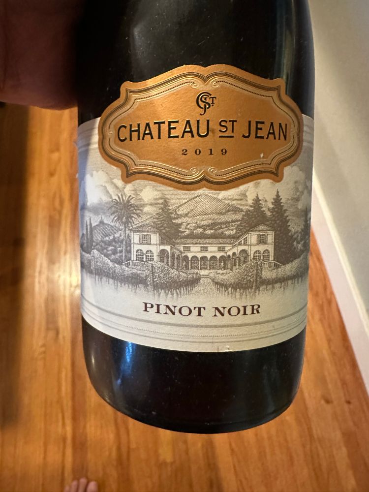The front bottle of a Pinot Noir with the label Chateau St Jean 2019 and the words Pinot Noir in the bottom part of the label.

On the label is a black and white illustration of a building that looks like a mission style building with vineyards in the foreground and a mountain in the background.