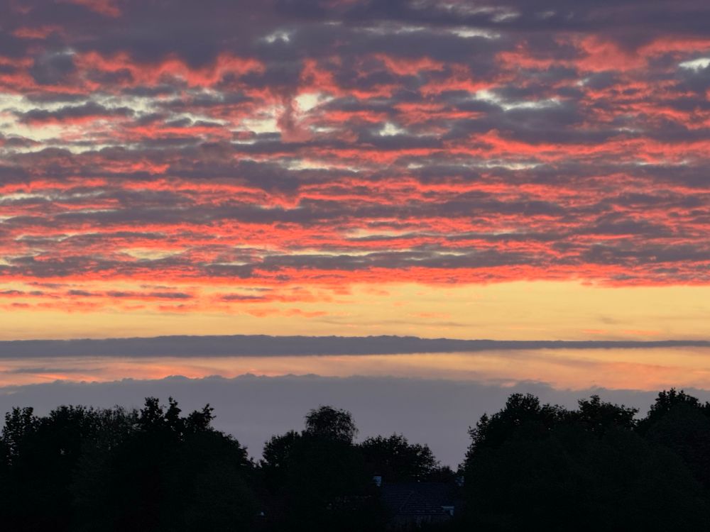 Ondergaande zon in Brabant met rode wolken omdat de zon de wolken aan de onderkant belicht 