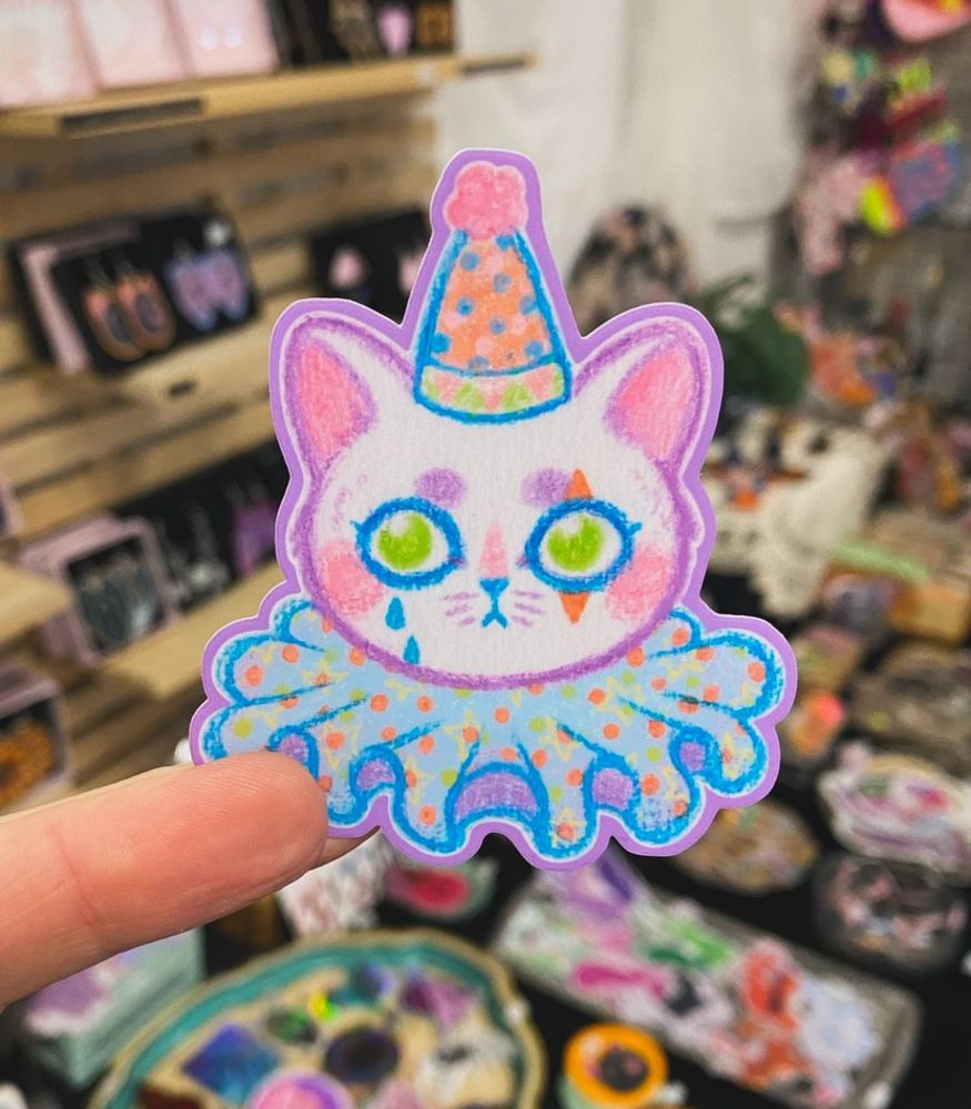 An illustration of a cute clown cat. The cat is wearing a little clown har and a collar.