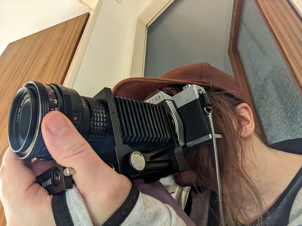 Some dude holding a Praktica super TL 2 SLR camera with bellows.