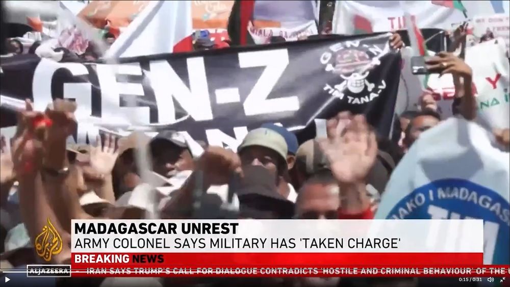 Imagen de las protestas en Al Jazeera, se ven cabezas de gente y una pancarta negra con las letras GEN-Z y una calavera con tibias cruzadas y caso militar, donde pone GEN-Z y ebajo TIM TANA-V

El rótulo dice "MADAGASCAR UNREST 
ARMY COLONEL SAYS MILITARY HAS "TAKEN CHARGE"