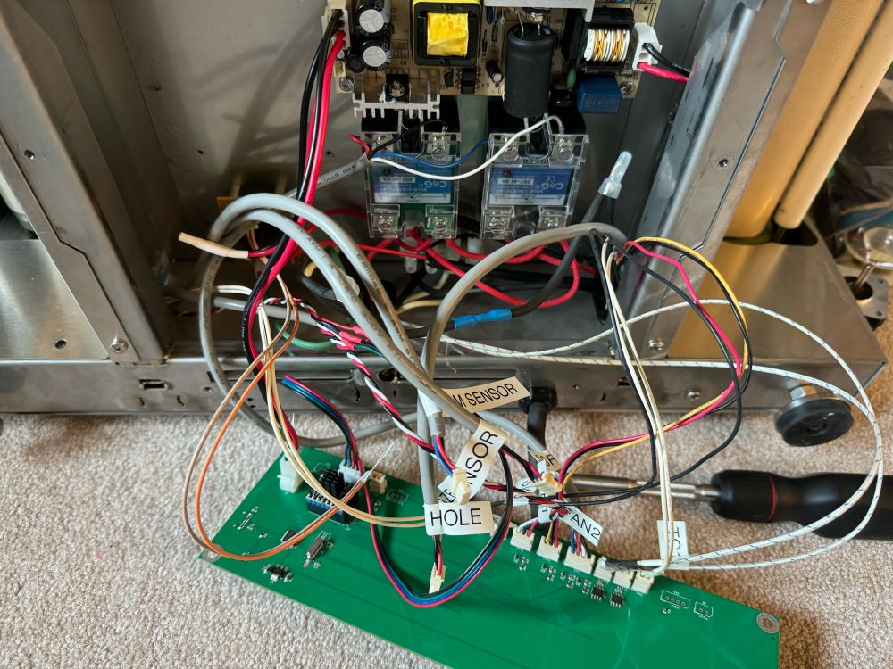 The bottom of a pancake machine with the electronic guts spilling out. A green circuit board has been wired to all the internals of the machine.