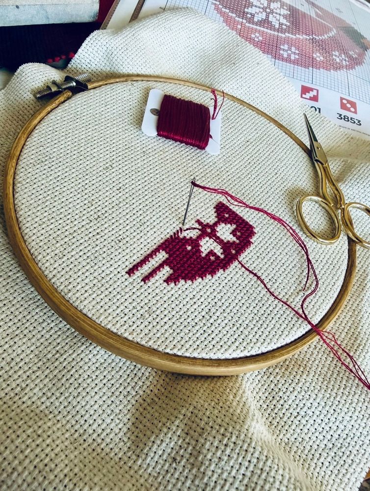 Start of a cross stitch project. So far there’s a small portion of maroon stitched in the embroidery hoop with negative space that is looking like a snowflake. 