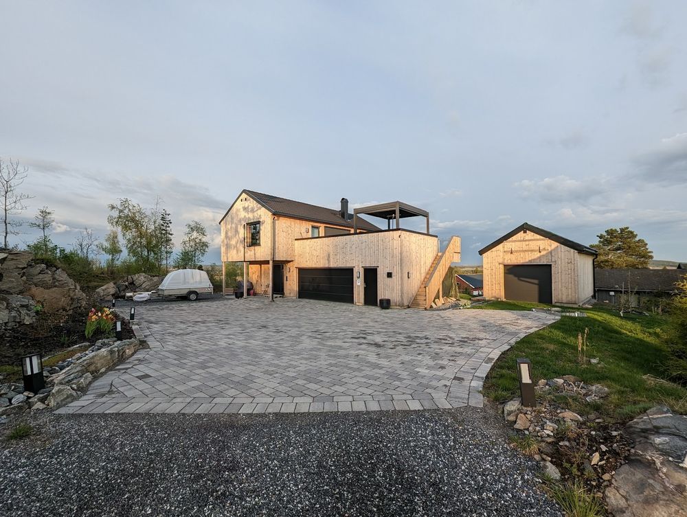 A wood paneled, unpainted, two story house, with a large garage with a patio on top, and a small garage next to it. 