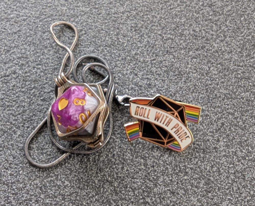 A d20 in the ace colors in a pendant for a necklace, and a "roll with pride" pin.