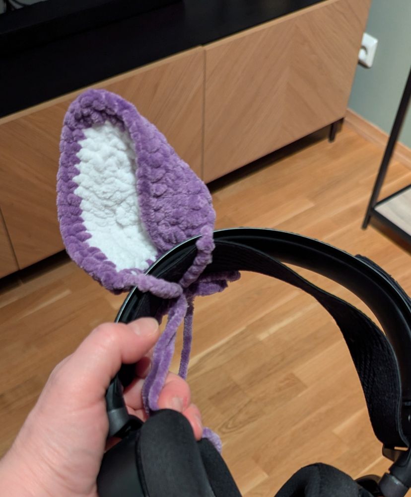 A black headset with a crocheted white and purple ear attached.