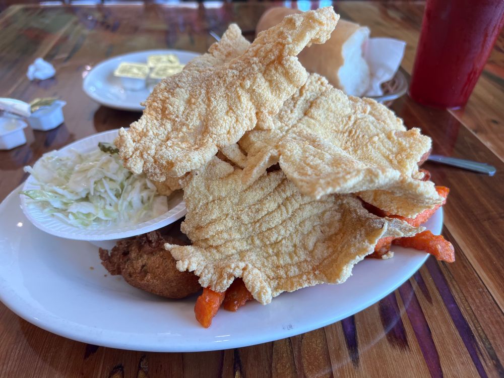 A plate with thin fried catfish, coleslaw, hush puppies & sweet potato fries. 