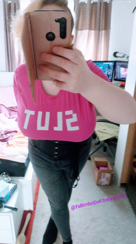 A shot of Doll leaning towards camera, it's fat fake udders hanging down and stretching it's shirt, letting the "SLUT" printing on it be read easily, telling y'all to treat Doll as nothing but whatnot marks itself as: A slut~