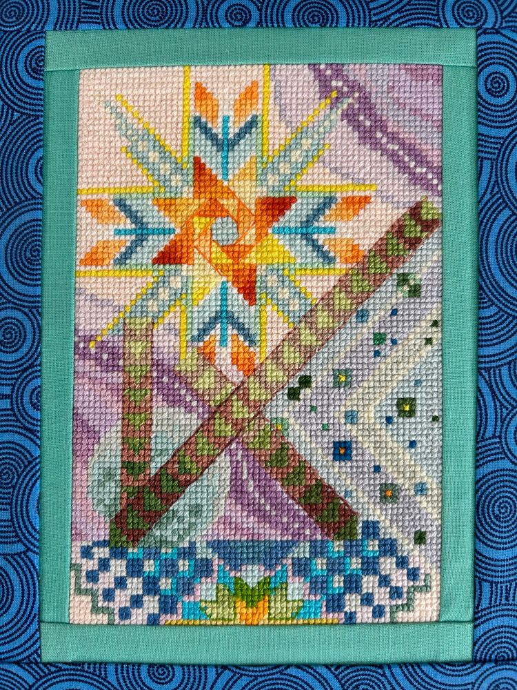 Yellow and orange star quilt block as central feature. Lavender and pale blue spacey background with pale blue planet, and green and brown arrow strips running diagonally across the background. 