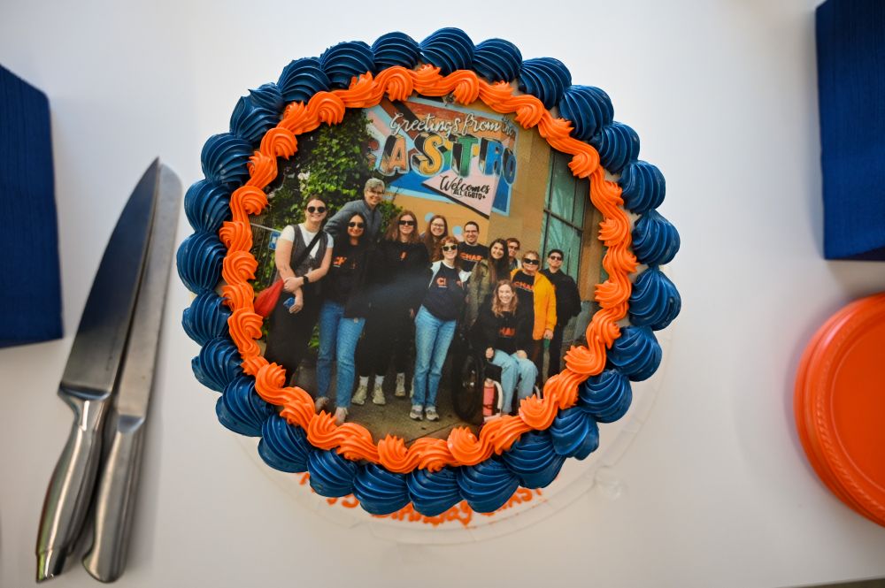 Photo of a cake. It has a group photo of members of the CHASI team printed on it. Many people in the photo are wearing CHASI sweaters, and they're posing in San Francisco in front of a sign in the Castro district. Around the edges are decorative icing in CHASI's signature orange and blue.