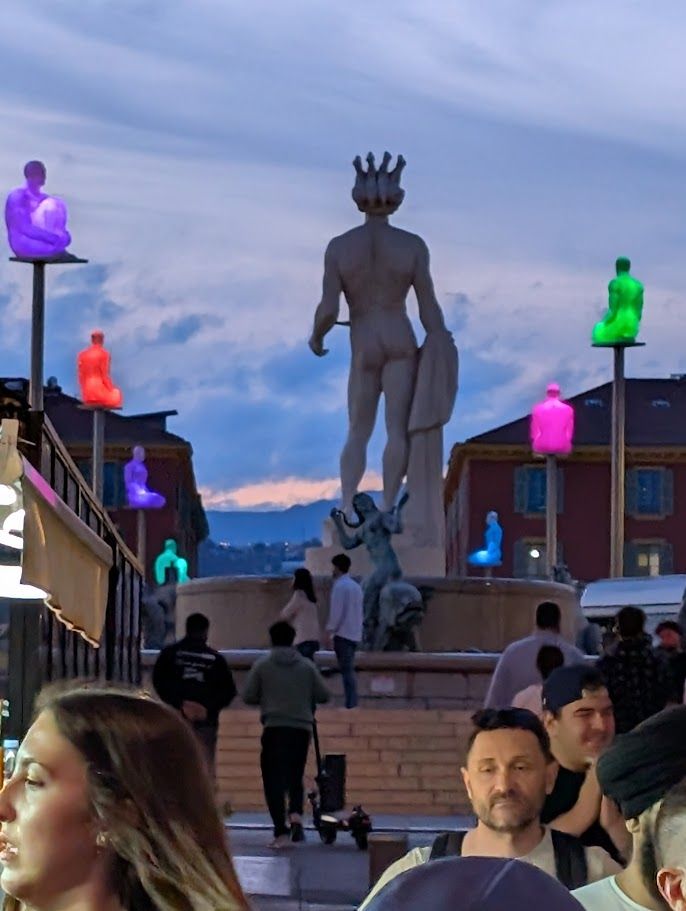 A classical statue surrounded set in a plaza with dozens of colorfully illuminated figures. 