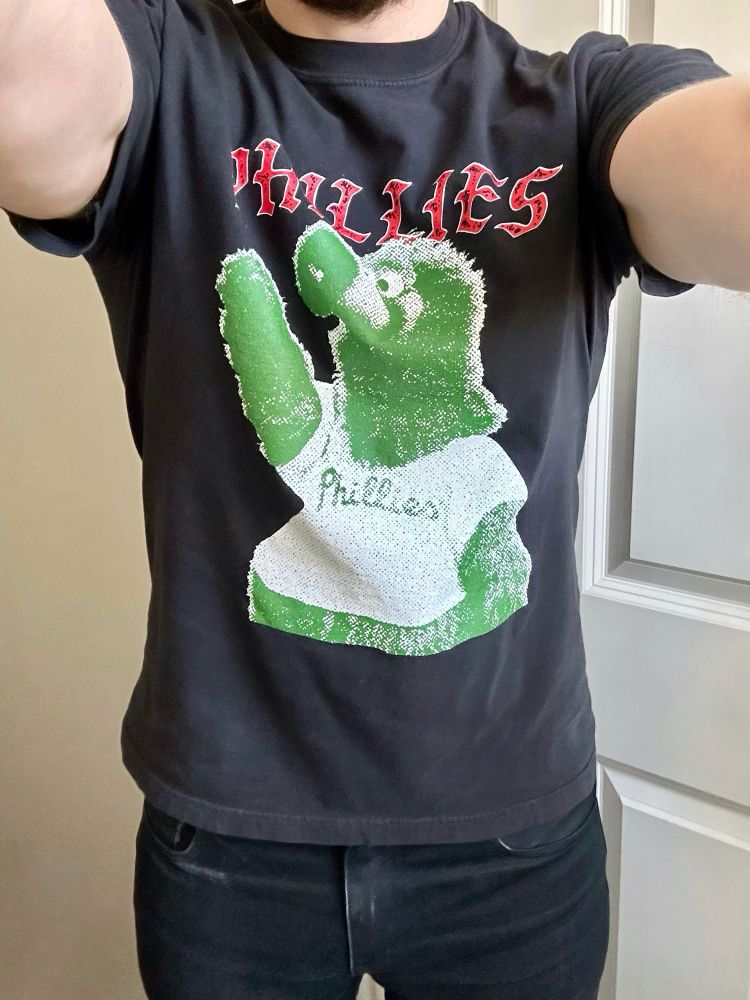 A man wearing a kick-ass black T-shirt featuring a halftone Phillie Phanatic with the word “Phillies” written above it in a metal-looking font