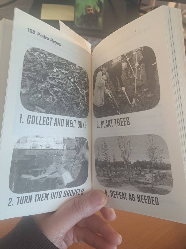My hand holds open a paperback displaying a page about Pedro Reyes' project. The page outlines a four-step process with black-and-white images: (1) Collect and melt guns, (2) Turn them into shovels, (3) Plant trees, and (4) Repeat as needed. The images visually depict each step, with piles of guns, a metalworking process, people digging, and newly planted trees. 