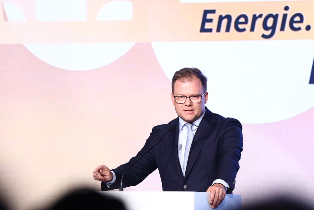 Ein Mann im dunklen Anzug und heller Krawatte spricht an einem weißen Rednerpult. Er trägt eine Brille und blickt ernsthaft ins Publikum. Im Hintergrund ist ein grafisch gestalteter Schriftzug mit dem Wort ‚Energie‘ zu sehen.
