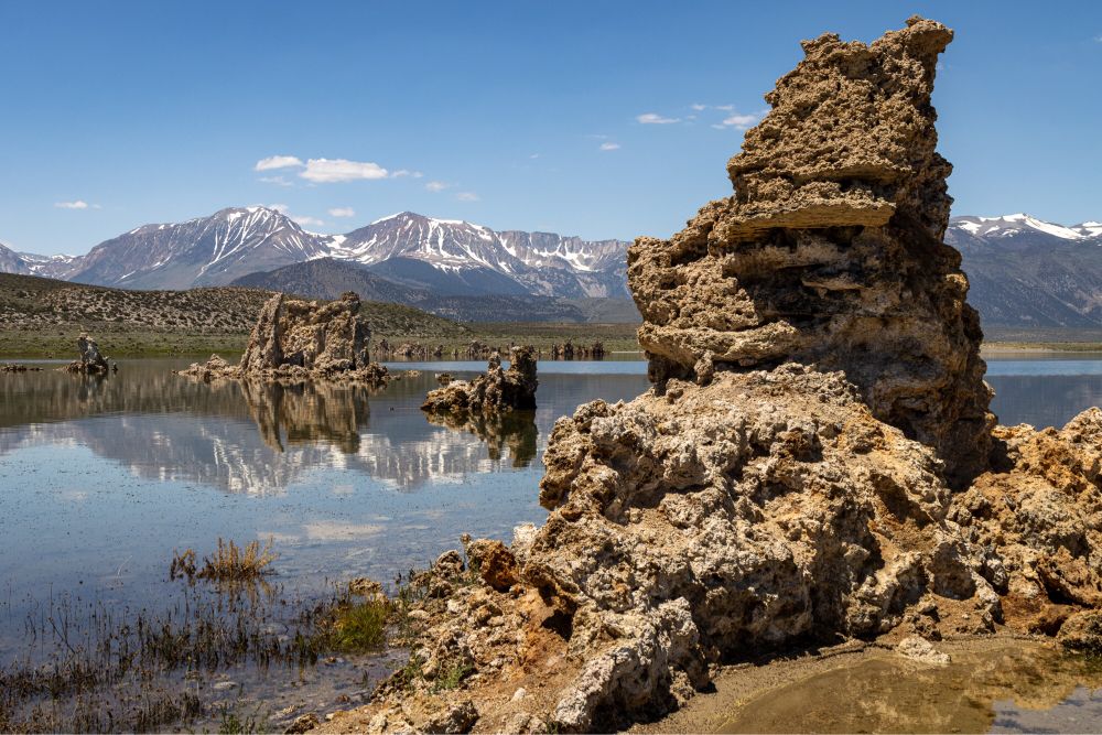 Mono Lake tufa reflections in the still lake water with a snowy Sierra mountain range in the background on a hot, sunny July day.