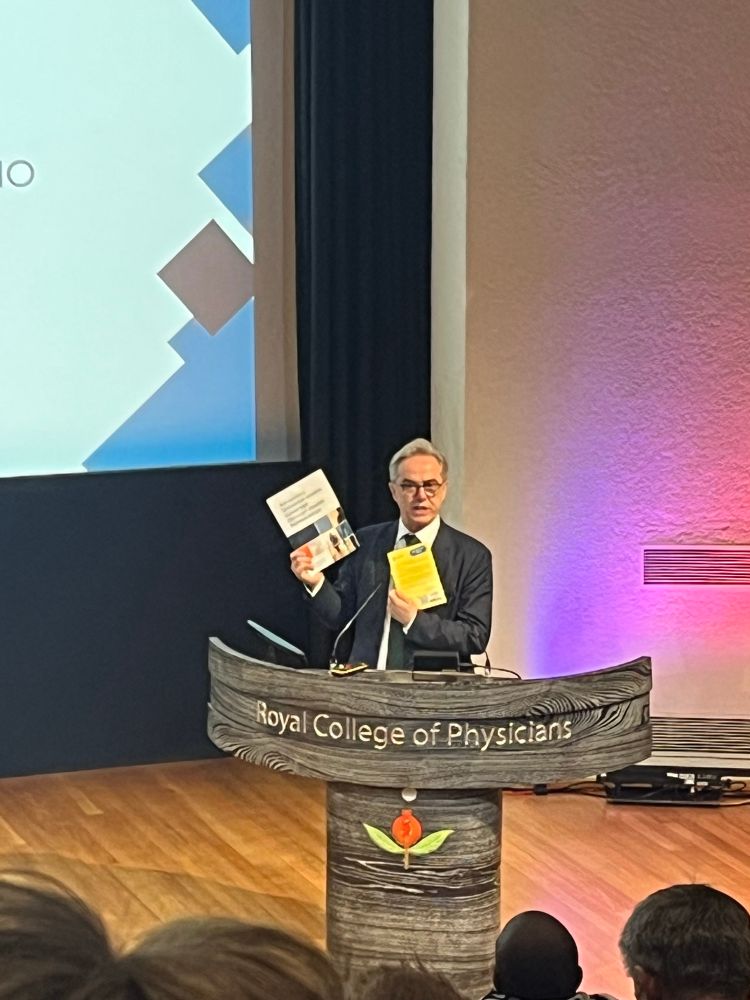 Dr. Jim Campbell of WHO standing at podium showing Global Health Partnerships (formerly THET) report on universal health coverage. 