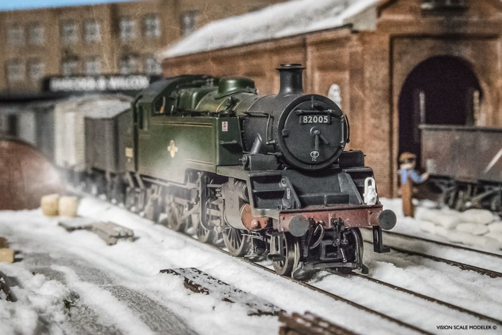 On an cold winter's morning, just as the sun is piercing through the gray sky, a weathered Bachmann 3MT quietly steaming through the yard with a train of kit-built wagons full of produce to market. This diorama is detailed with Woodland Scenics snow on a pastel paper and foam base, with Scenecraft and Walthers structures in the background.