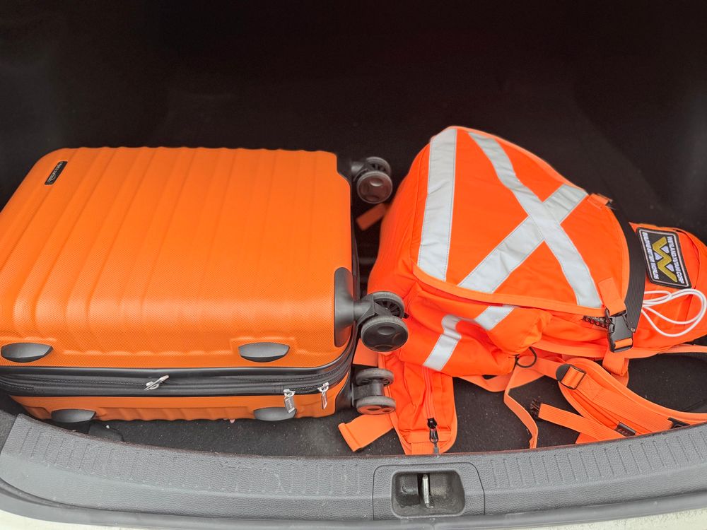 An orange hard-shell carry-on and a hi-viz orange backpack in the boot of a cab.