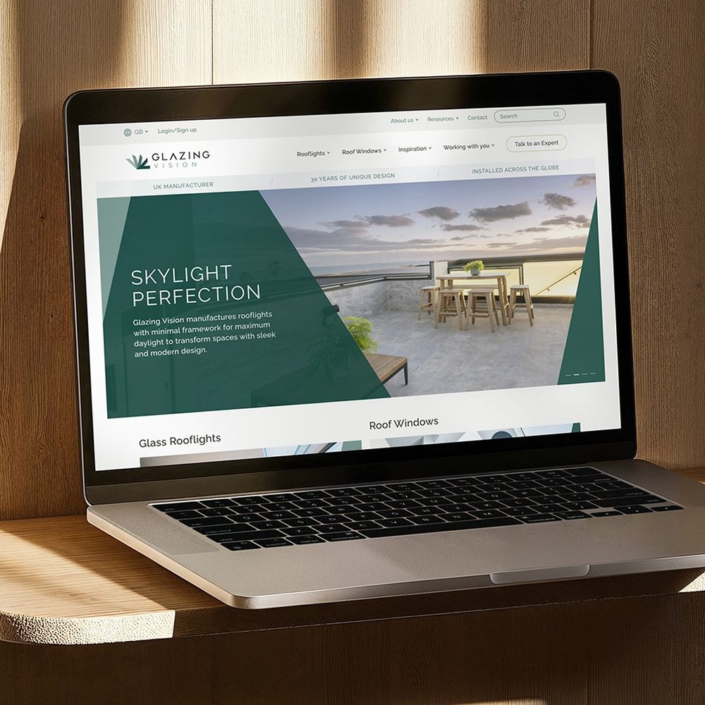 A laptop displaying the homepage of the Glazing Vision website, featuring an outdoor rooftop space with a skylight, a dining table, and chairs. The page highlights "Skylight Perfection," noting Glazing Vision as a "UK Manufacturer" with "30 Years of Unique Design," and "Installed Across The Globe." The top navigation shows links for "Rooflights," "Roof Windows," "Inspiration," and "Working with you."