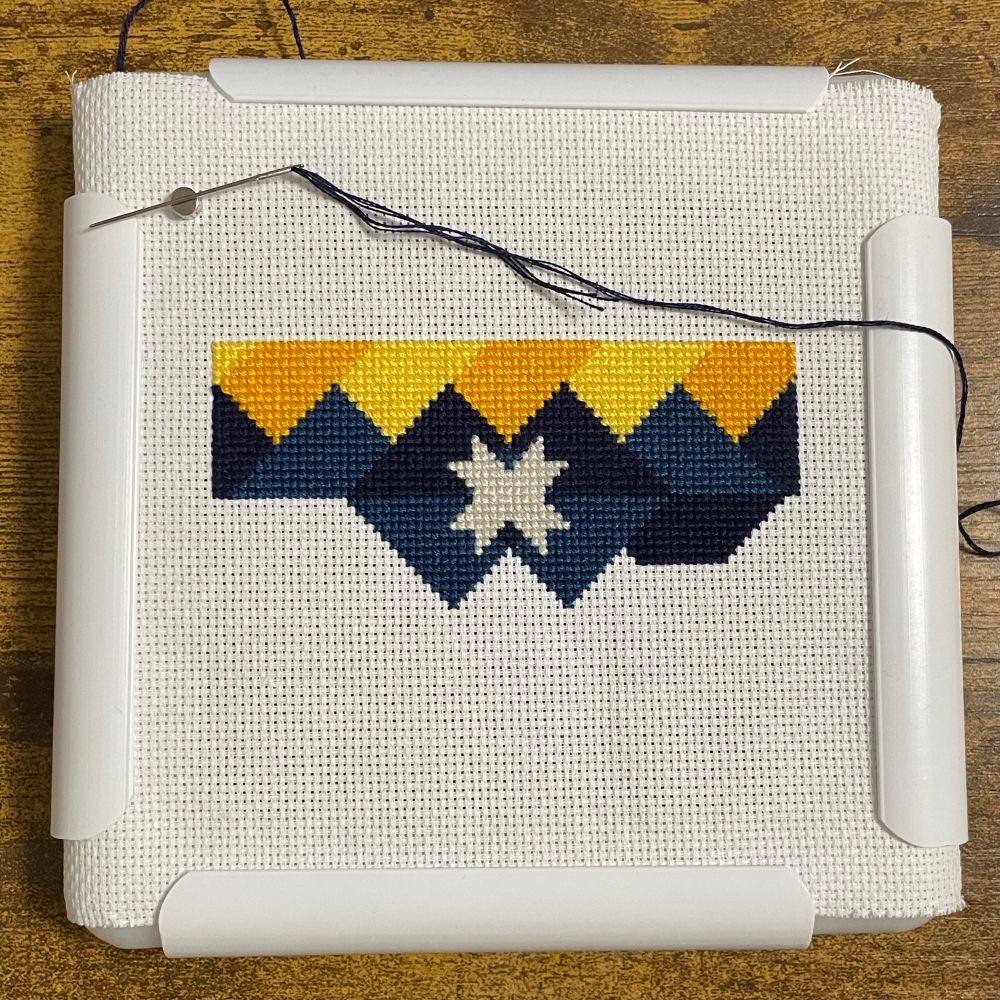 A photo of a cross stitch project. The image depicted in the cross stitch is part of the unofficial Appalachian flag. The project is inside a Q snap frame.