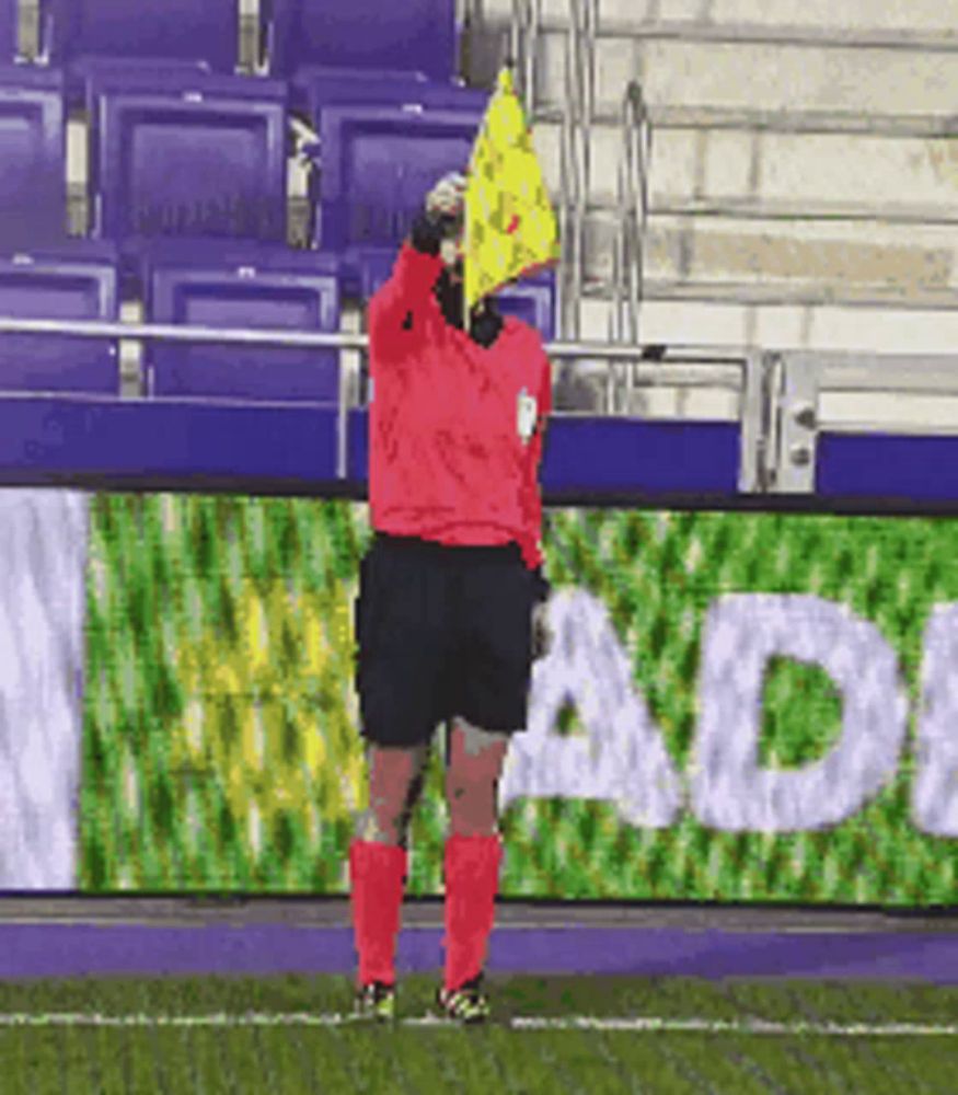 a soccer referee is holding a yellow flag in front of a sign that says adi