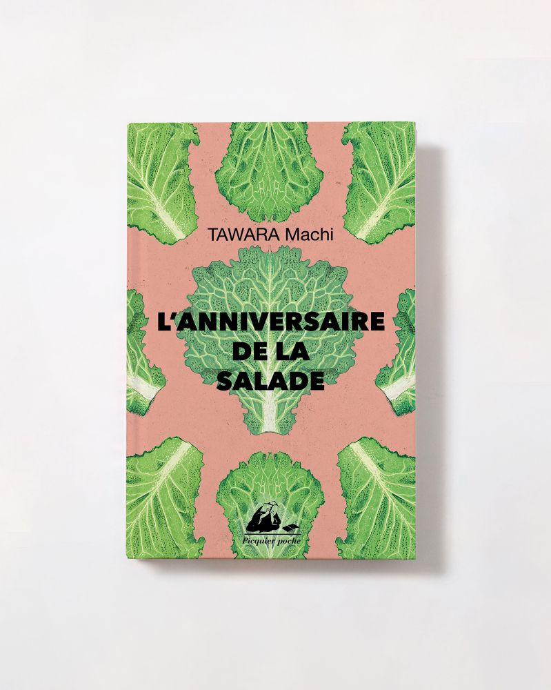 Book cover with detailed, textured Illustrations of lettuce in a repeat pattern on pink background. The book cover has ‘l’anniversaire de la salade’ in black text. The book is on a white table.