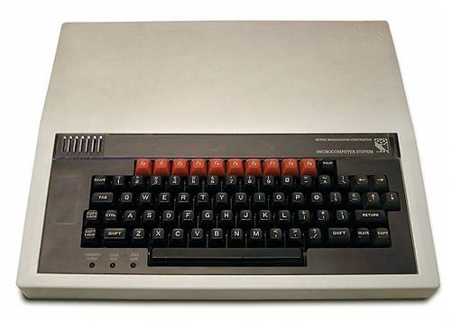 Image of a BBC micro computer from the 80s. It's so very beige. Basically a chonky keyboard that extends out as a brick to hold the actual computer. The logo is an adorable little pixelated owl 