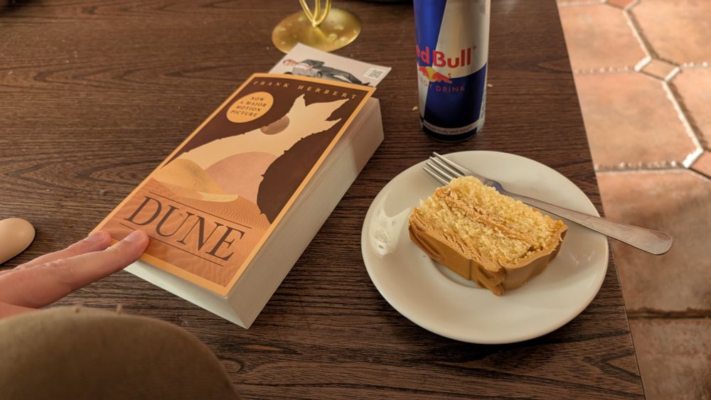 A copy of dune in paperback, a redbull and a slice of cake