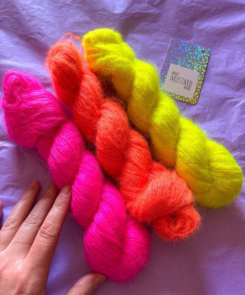 Theee twisted skeins of bright neon mohair in pink, coral orange, and yellow. 