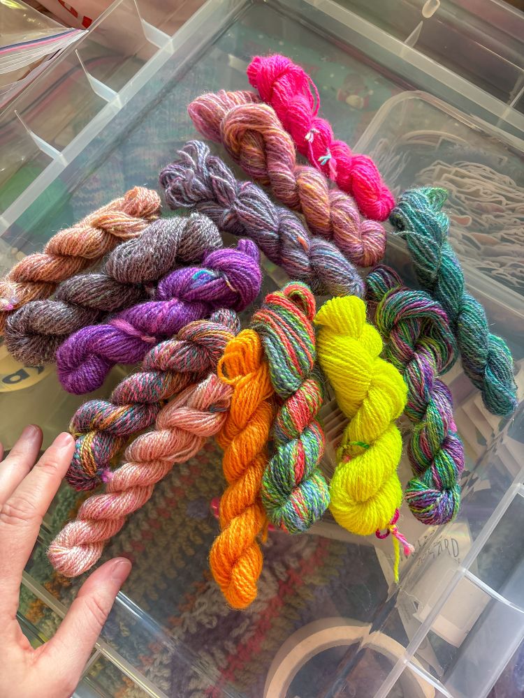 13 tiny skeins of handspun* yarn sitting looking pretty. There are many colours - neon pink, orange, and yellow semi-solids, and the rest are all variegated in various colours:  purples, blues, greens, peaches, oranges. 

* autocorrect wanted that to say handsome. I don’t actually disagree, they are handsome! 🥰 