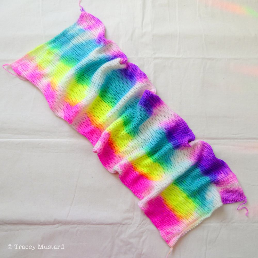 A top-down of a hand dyed sock blank. This blank has been dyed rolled up, with a neon rainbow applied sideways on top of the roll in (all neon dyes) Pink on one side, into Orange, Yellow, Green, Aqua Blue, Lavender, and ending with Purple. There are lighter and darker saturation sections, and undyed parts, due to the way they were dyed rolled up. As the dye doesn't reach all the way into the middle, one end of the blanks will have more saturation than the other because of this. I think this will work up incredibly interestingly...! I'd love to keep one for myself so I can see how it'll work up in something, but these babies must earn their keep, so none for me!