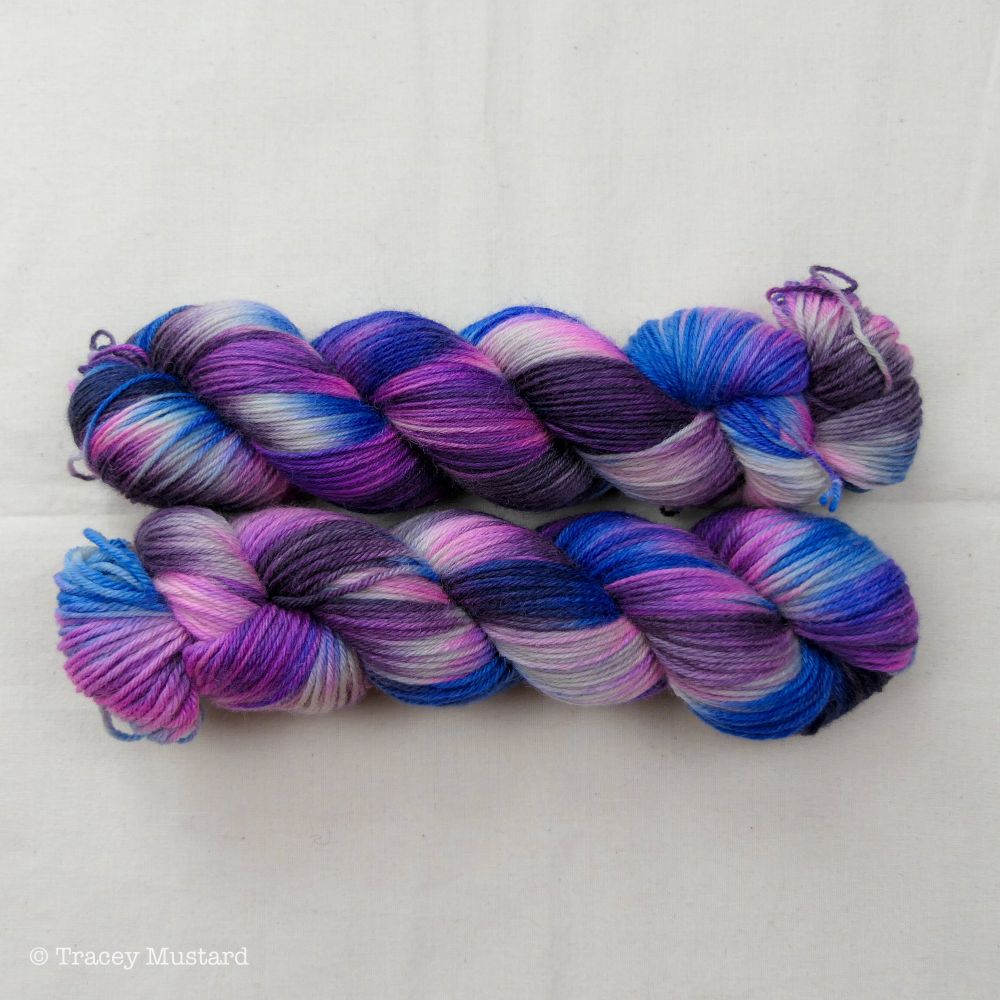Two skeins of twisted yarn, in variegated dark neon purple, brown, and bright indigo blue.