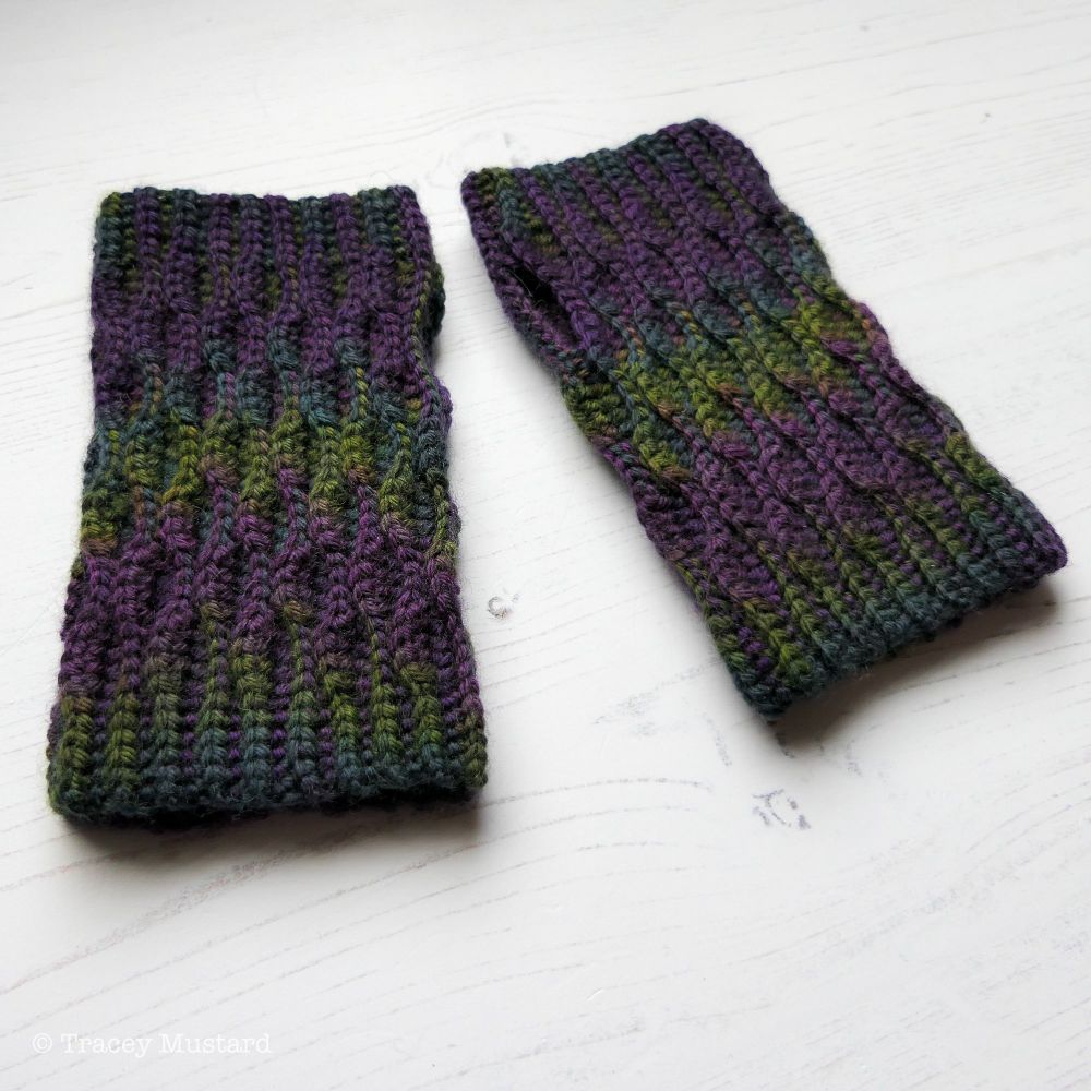 A shot of a pair of crocheted fingerless gloves made in Voidbow dark neon rainbow yarn. The colours move through the gloves in a very pleasing way, which looks a little bit like spilt petrol.