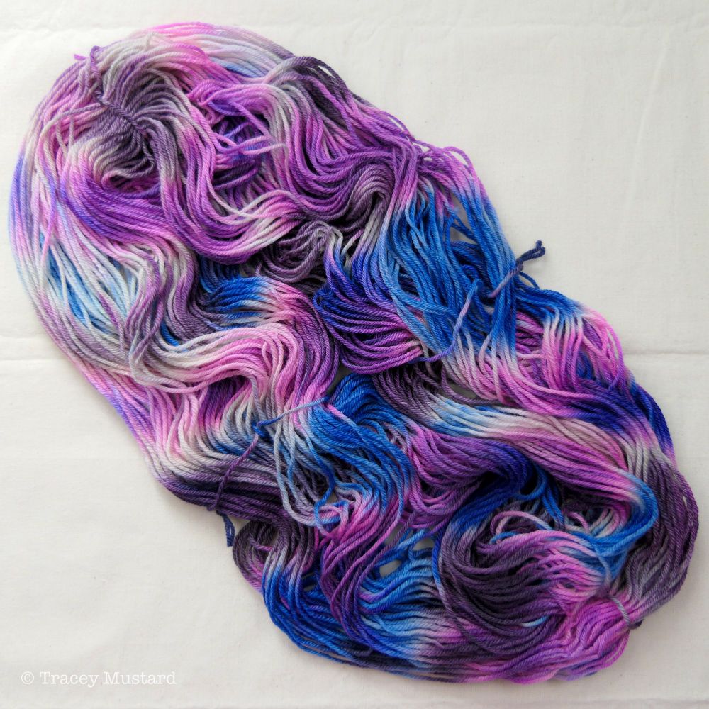 A skein of DK yarn laid out flat, in variegated dark neon purple, brown, and bright indigo blue.