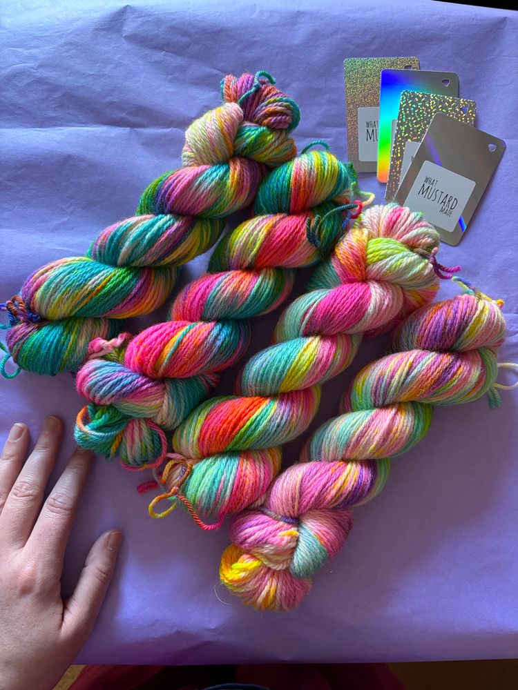 Four twisted skeins of variegated hand dyed Aran Bluefaced Leicester yarn, in various pinks, purples, and blues, with yellow speckles creating oranges and greens. 