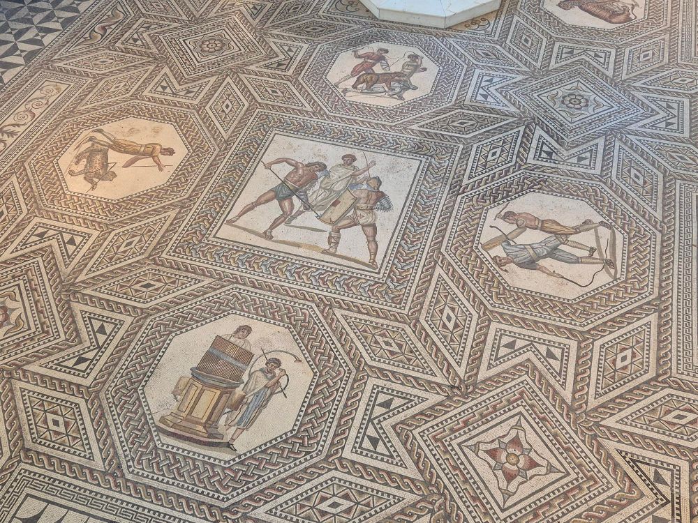 Detail of the mosaic with various images of fighting gladiators. In front an octogon with an image of two musicians, a water organ and a horn. 