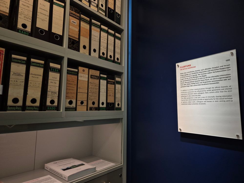 Blick in die Ausstellung: rechts der Wandtext zum Thema "Flurfunk", links das Foto eines Aktenschranks. 