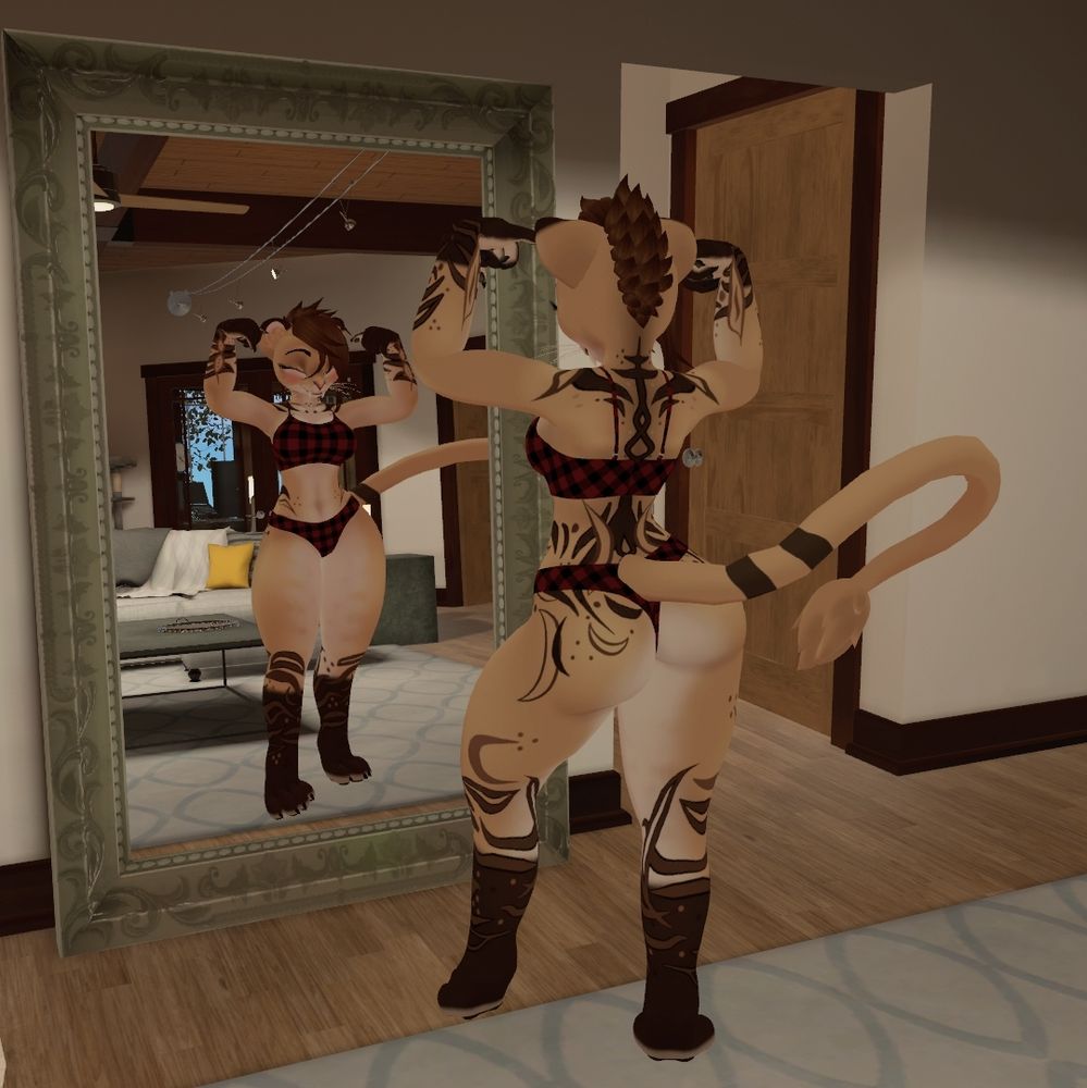 The picture is from behind the subject and shows her front in a mirror. z's chibi lioness avatar is looking in the mirror flexing her biceps. She's only wearing flannel underwear and smiling