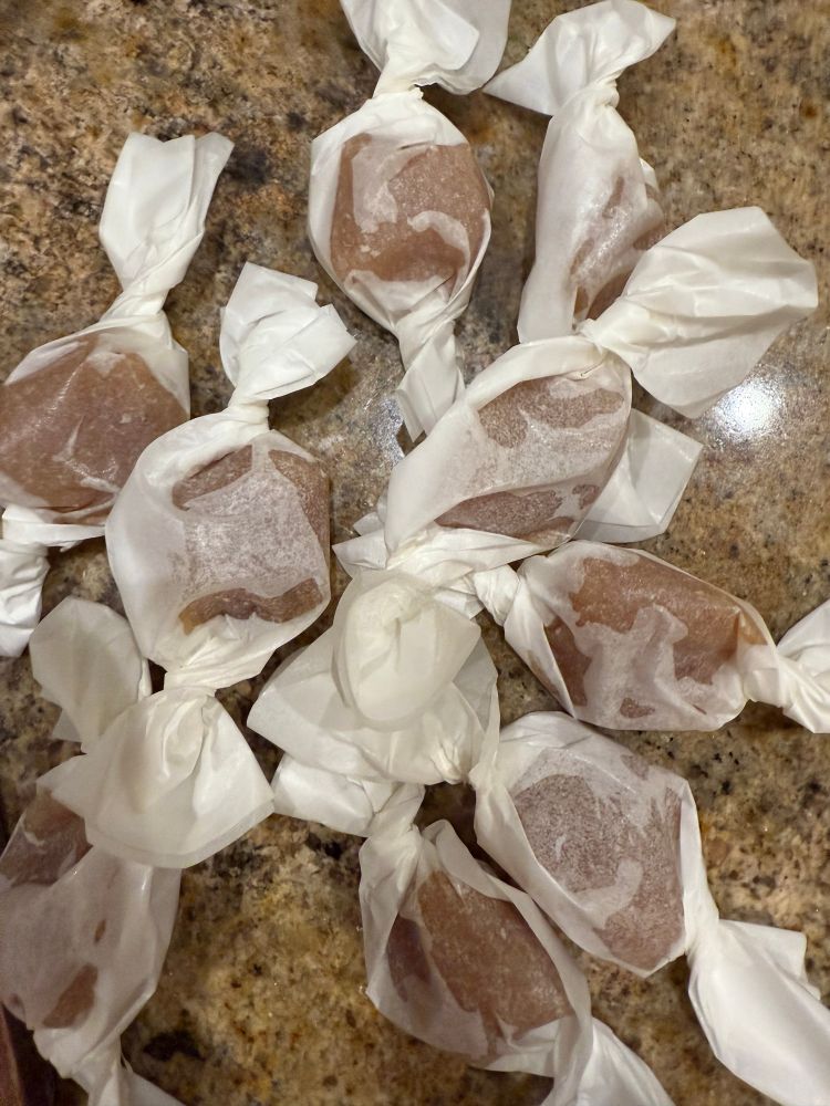 Eight one-inch square apple cider caramels, wrapped in wax paper squares. 