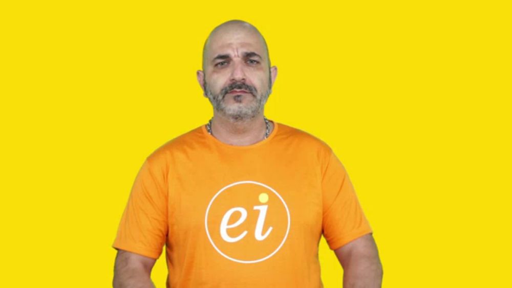 a man in an orange shirt is pointing at his watch in front of a yellow background with clocks