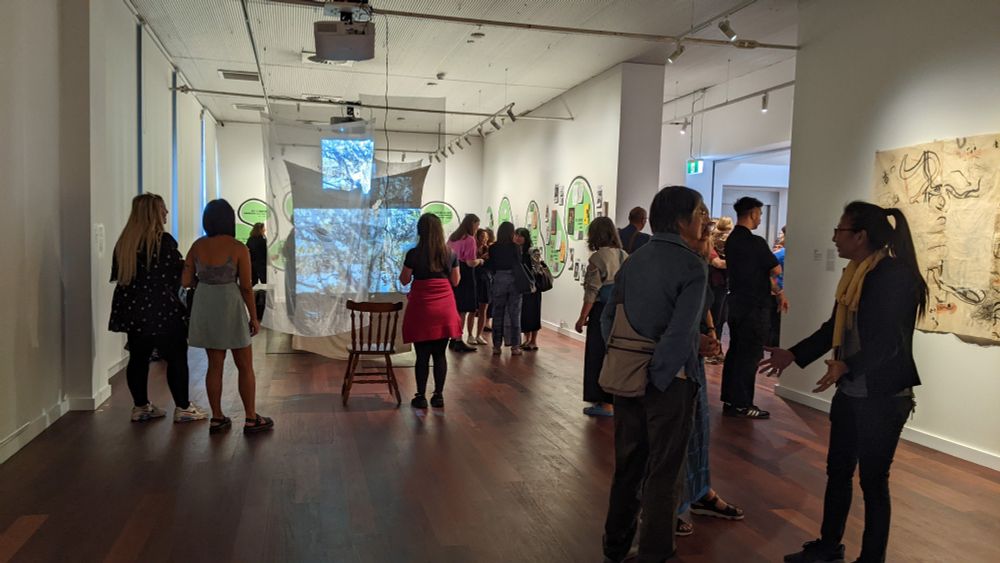 Gallery space filled with people and both hanging and wall mounted artworks,