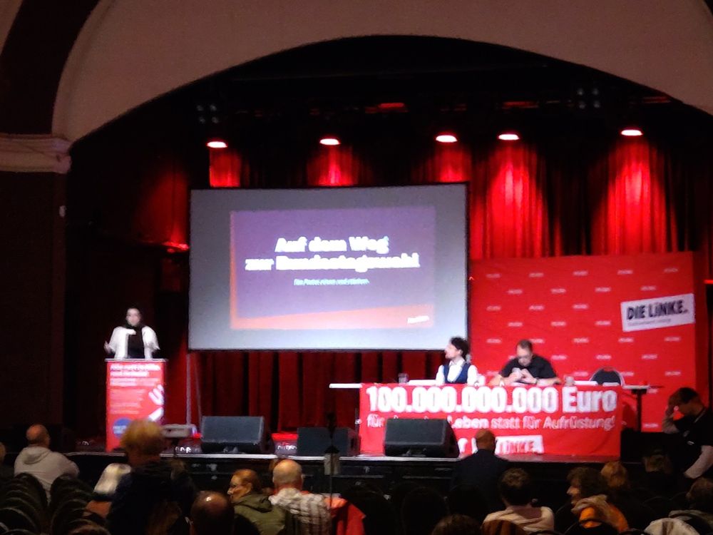 Bühne im Felsenkeller Leipzig.

Links, das Podium, daran steht Franziska. Rechts im Bild, das Präsidium, mit Sören Pellmann und einem weiteren Genossen.

Dahinter, groß, breit der Monitor mit einer Folie: "Auf dem Weg zur Bundestagswahl"