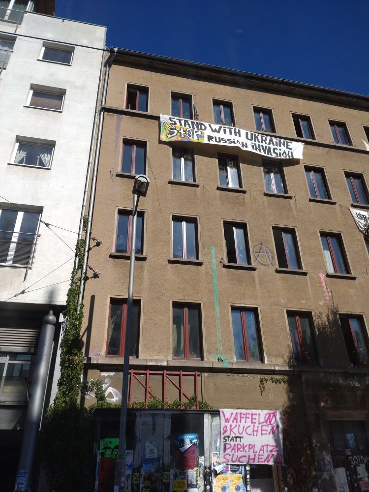 Fassade eines Hausprojekts, Eisenbahnstr., Leipzig.
Offener alter / unsanierter Putz, hier und da ein A im Kreis als Graffiti.

Ein Transpi, 4. Stock: 
STAND WITH UKRAINE
STOP RUSSIAN INVASION

Ein anderes Transpi, Erdgeschoss:
Waffeln und Kuchen
Statt Parkplatz suchen.

Das N in "KUCHEN" ist in einem Kreis mit Pfeil nach draußen. Das Transpi ist offenbar noch übrig vom Parking Day, dem gestrigen Protesttag für mehr Freiraum statt Park- und Verkehrsfläche in öffentlichen Räumen. 