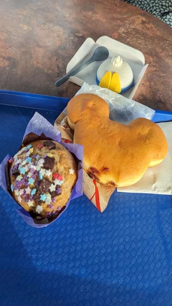 A variety of snacks, a muffin with colorful, star shaped sprinkles, a donut in the shape of Micky Mouse and a Mousse in the shape of Donald Ducks bum.