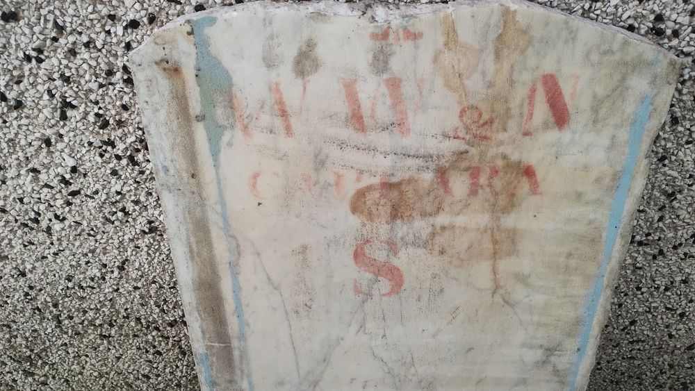 Smooth stone slab in cream with red and light blue paint - letter S visible under what looks like “w w & n” 