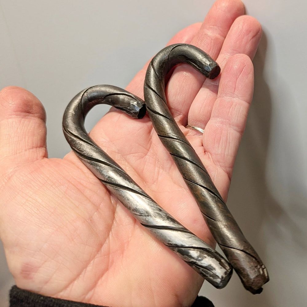 Two steel candy canes held in the palm of a person's hand.