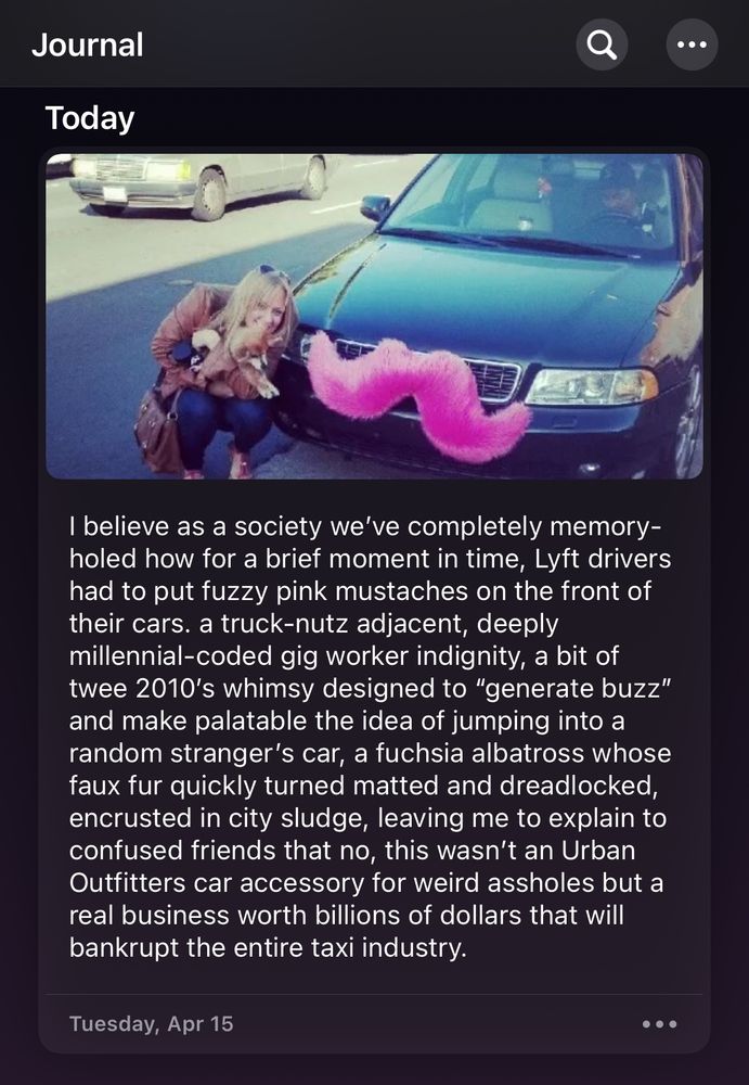 Screenshot of the journal app, pic of a woman crouching next to a car with a pink fur mustache on the grill. Text reads: “I believe as a society we’ve completely memory-holed how for a brief moment in time, Lyft drivers had to put fuzzy pink mustaches on the front of their cars. a truck-nutz adjacent, deeply millennial-coded gig worker indignity, a bit of twee 2010’s whimsy designed to “generate buzz” and make palatable the idea of jumping into a random stranger’s car, a fuchsia albatross whose faux fur quickly turned matted and dreadlocked, encrusted in city sludge, leaving me to explain to confused friends that no, this wasn’t an Urban Outfitters car accessory for weird assholes but a real business worth billions of dollars that will bankrupt the entire taxi industry.”