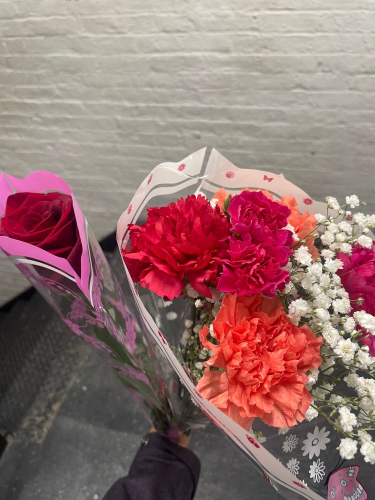 i am holding a single red rose, and a small bouquet of red, pink, and orange carnations with white babys breath. 