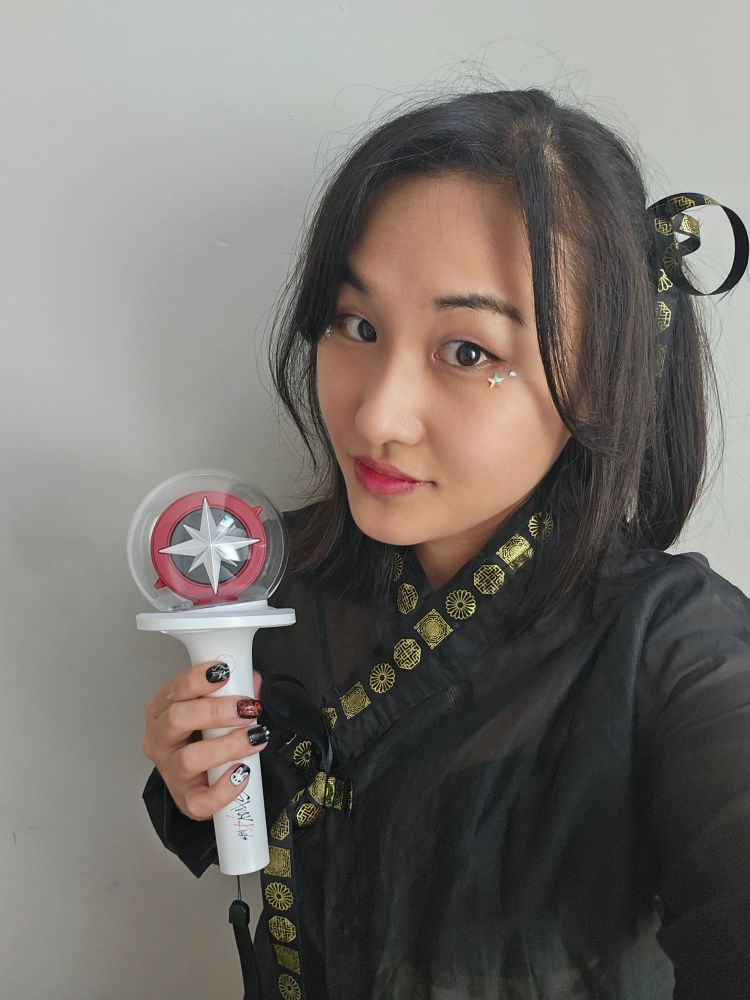 Korean girl dressed in black and gold modern hanbok inspired outfit. Holding a stray kids light stick